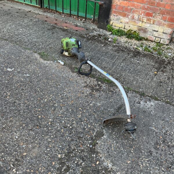 Used petrol garden strimmer with curved shaft for lawn maintenance.