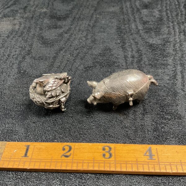 Vintage pewter bird and pig trinket pots on black fabric.
