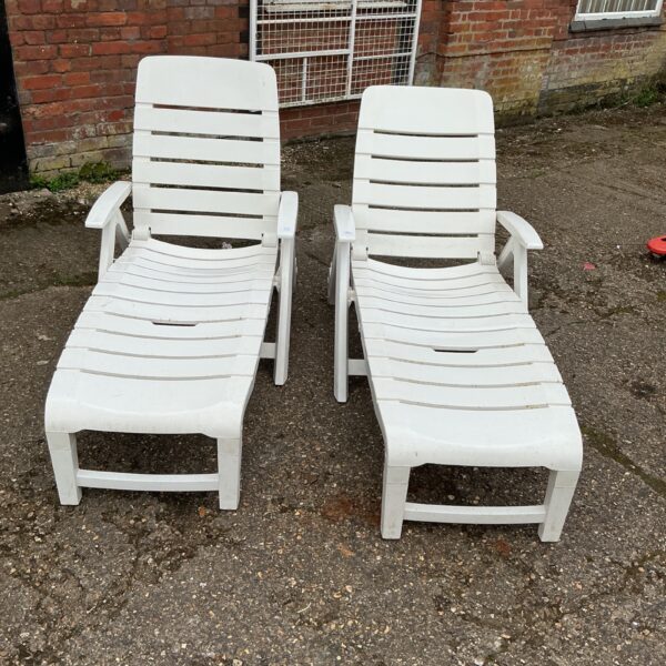 Two plastic sunloungers in a garden setting.