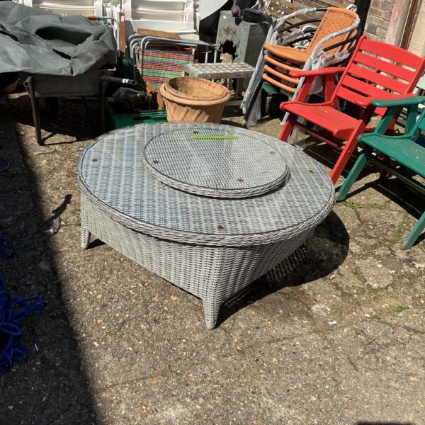 Round raffia garden table with glass top in outdoor setting.