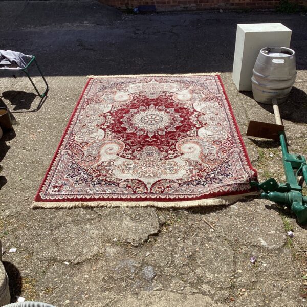 Red Arabic style rug with geometric pattern on a concrete surface.