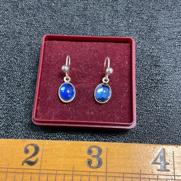 Close-up of sapphire blue drop earrings on a dark background.
