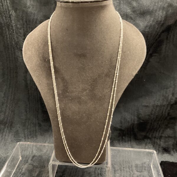 Two delicate silver ball link necklaces on a display stand.