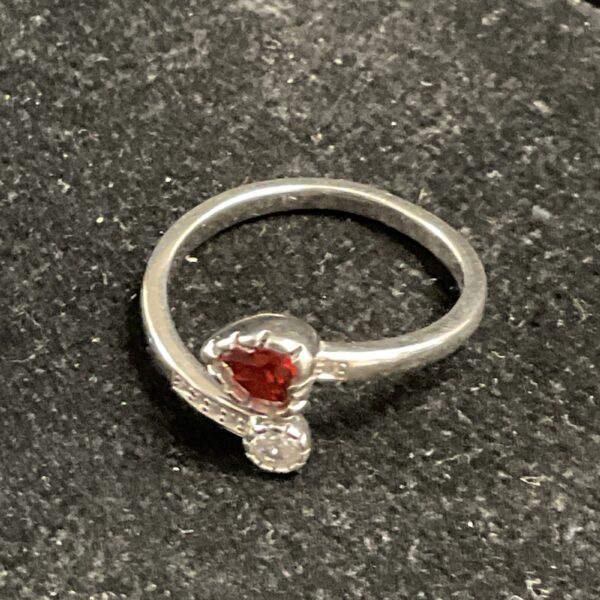 Silver ring with a red heart-shaped stone in a crossover setting.