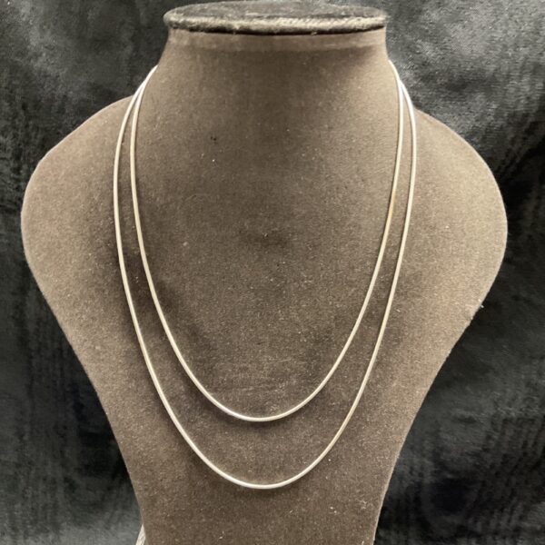 Layered silver snake chain necklaces on display.