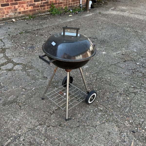 Small metal barbecue grill for outdoor cooking in a garden setting.