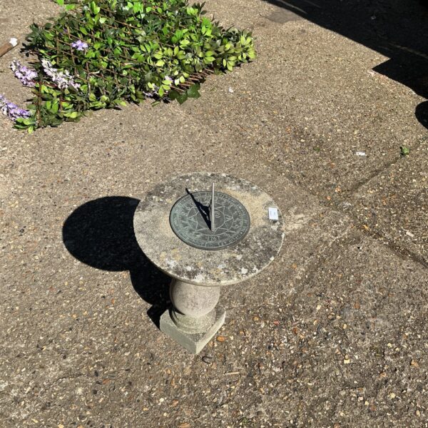 Classic stone garden sundial on a pedestal in a garden setting.
