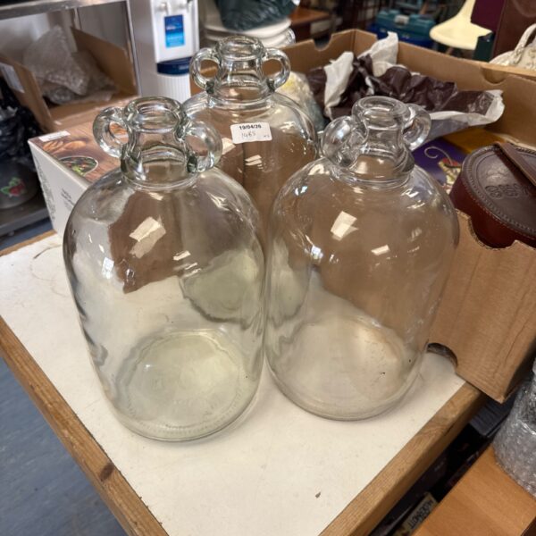 Three clear glass demijohns for fermentation and storage.