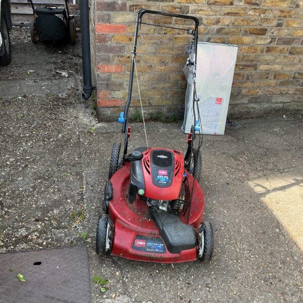 Red Toro petrol lawnmower with Recycler system in a garden setting.