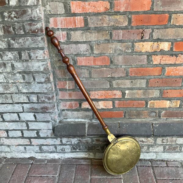 Vintage brass bed pan with embossed floral design and wood handle.