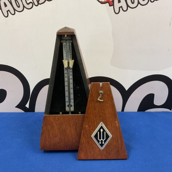 Side view of a vintage clockwork metronome with wooden casing.