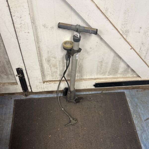 Vintage metal cycle pump with wooden handle on floor.