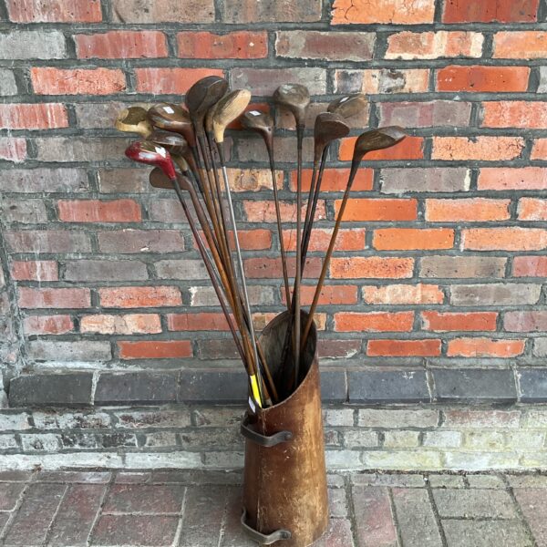 Vintage golf clubs with hickory shafts in a weathered coal scuttle.