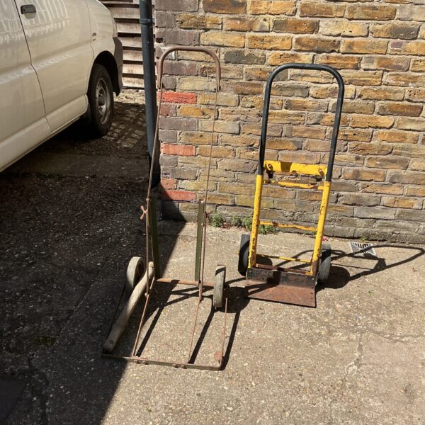 Two vintage metal hand trolleys needing repair in a garden setting.
