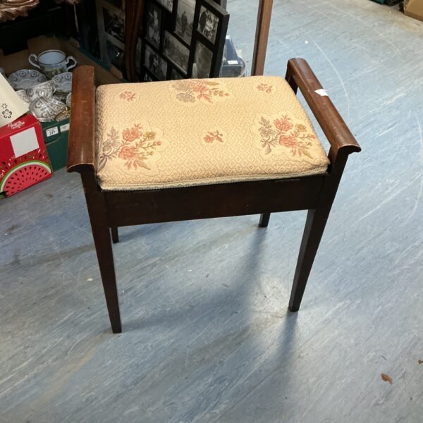 Front view of a vintage mahogany piano stool with patterned seat.