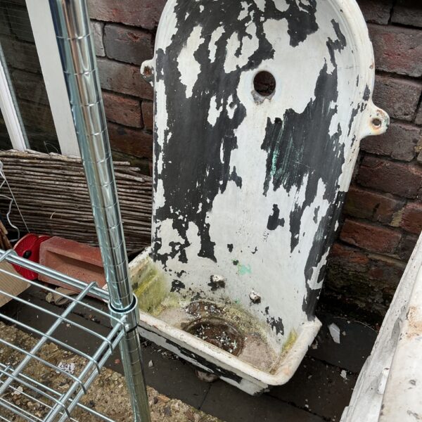 Vintage metal wall fountain with weathered patina in garden setting.