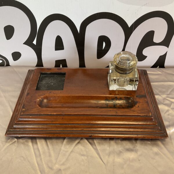 Vintage wooden pen stand with glass inkwell on a desk.