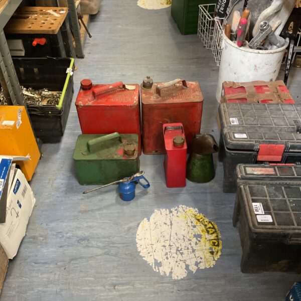 Collection of vintage petrol cans in a workshop setting.