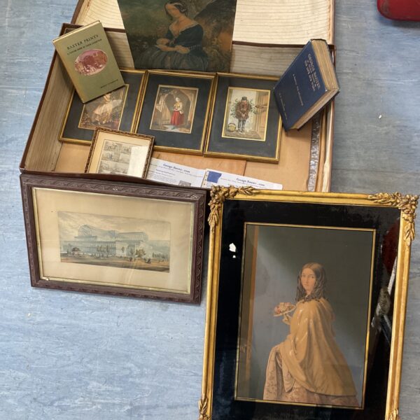 Vintage brown suitcase open with antique George Baxter prints inside.