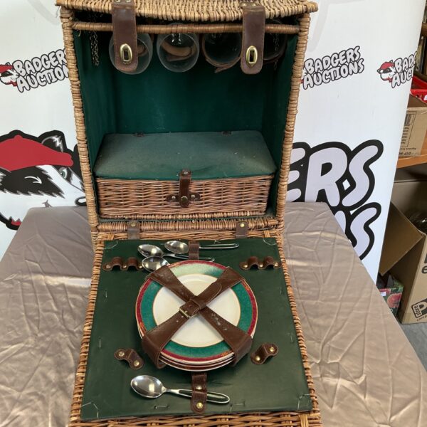 Vintage wicker picnic basket with plates and cutlery inside.