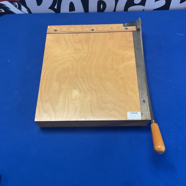 Front view of a vintage wooden paper cutter with metal blade.