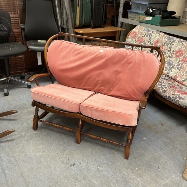 Pink vintage wooden settee with curved back and armrests.