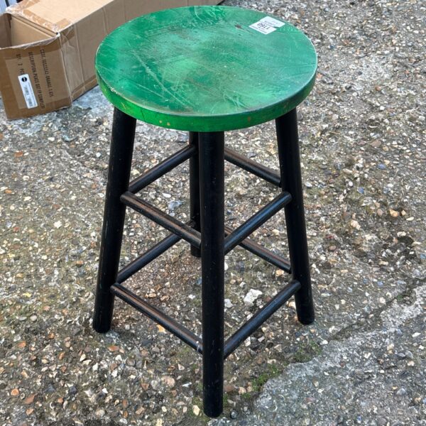 Vintage wooden store stool with green seat and black legs.