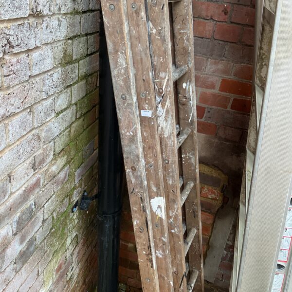 Vintage wooden triple ladder leaning against a brick wall.