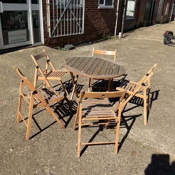 Vintage wooden patio set with five folding chairs in a garden.