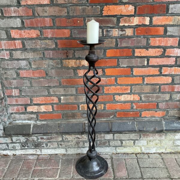 Antique bronze candlestick with twisted stem against brick wall.