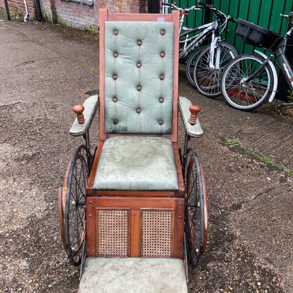 Antique wheelchair with green upholstery and wooden frame.