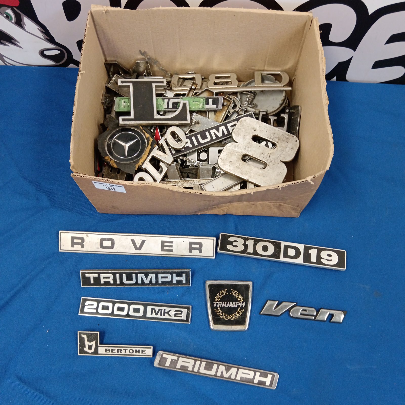 Vintage car badges collection featuring Triumph and Mercedes emblems.