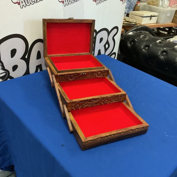 Open carved wooden jewellery box displaying red velvet lining.
