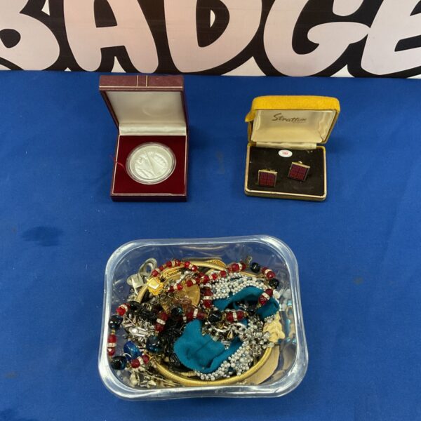 Costume jewellery lot with medal and cufflinks on blue surface.
