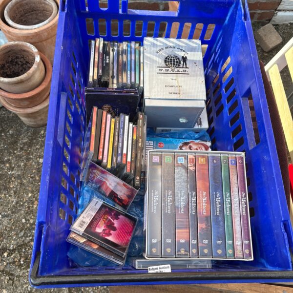 Blue crate filled with assorted DVDs and CDs for sale.