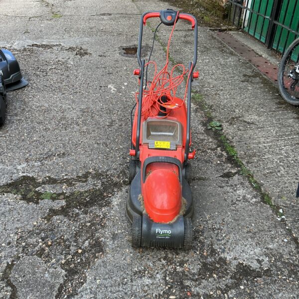 Red Flymo Chevron electric lawnmower in a garden setting.