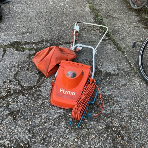 Vintage Flymo electric lawnmower with power cable in a garden setting.