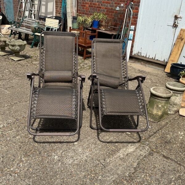 Pair of grey folding sunloungers in a garden setting.