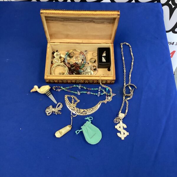Close-up of a gold-tone gangster dollar sign necklace in a jewellery box.