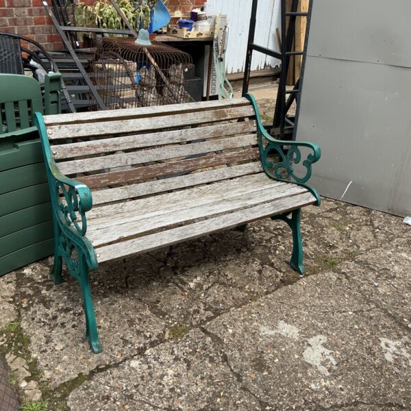 Green metal garden bench with wooden slats in a garden setting.