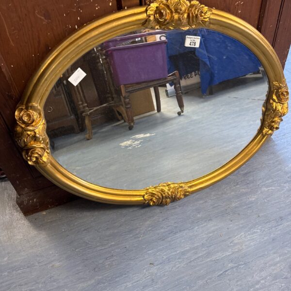 Ornate gilt framed oval mirror with detailed carvings.
