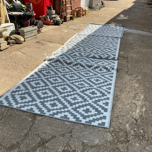 Three grey geometric patio mats in a garden setting.