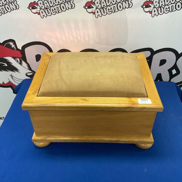 Front view of a light oak footstool with lift-top storage.