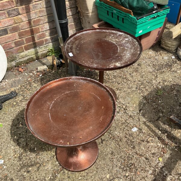 Pair of weathered metal garden tables in a garden setting.