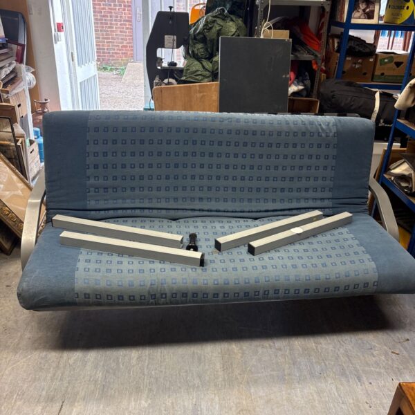 Vintage metal framed sofa bed in a cluttered room.
