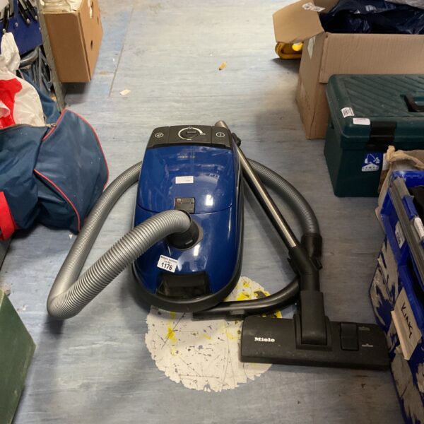 Side view of a used Miele vacuum cleaner with hose attached.
