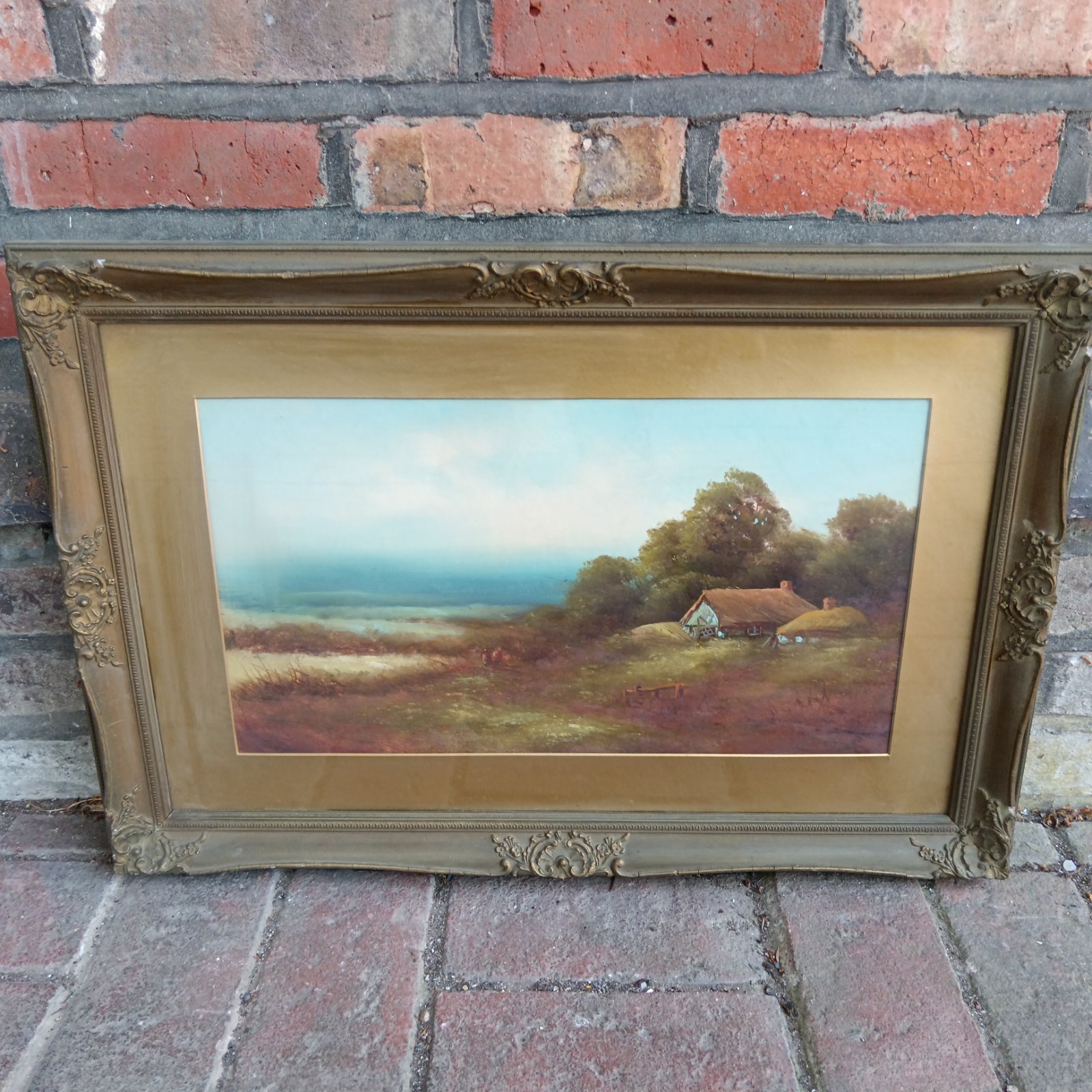 Gilt framed oil painting of a country cottage and rural landscape.