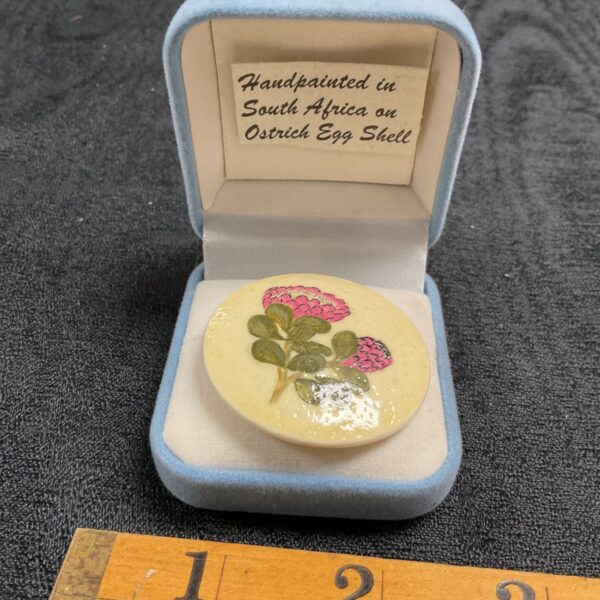 Close-up of a hand-painted ostrich egg brooch with floral design.