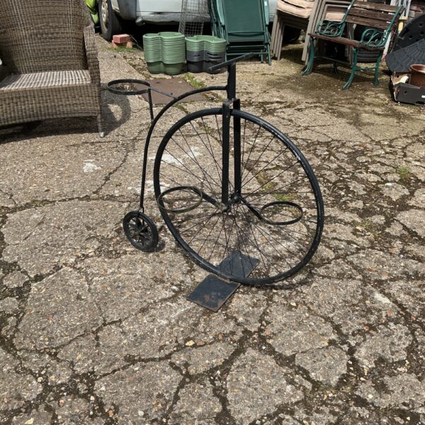 Metal penny farthing plant stand in a garden setting.