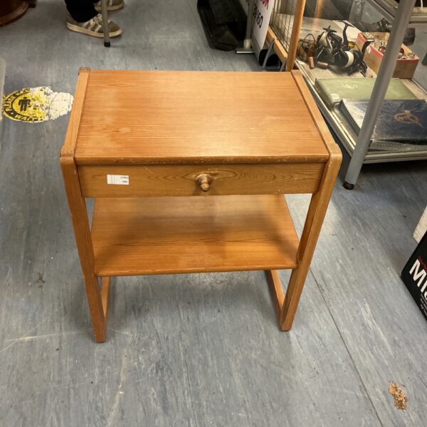 Small pine side table with drawer and shelf for bedside storage.